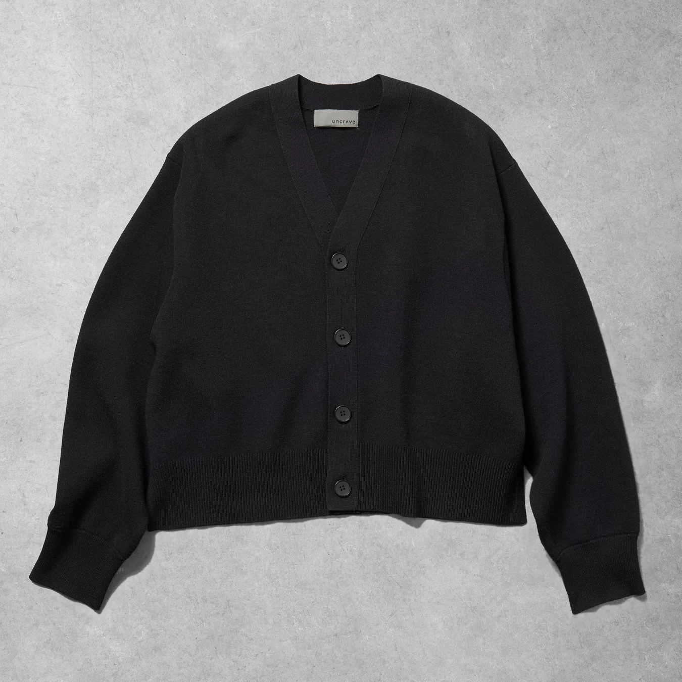 グレーの背景に平置きされた、黒いVネックのカーディガンです。