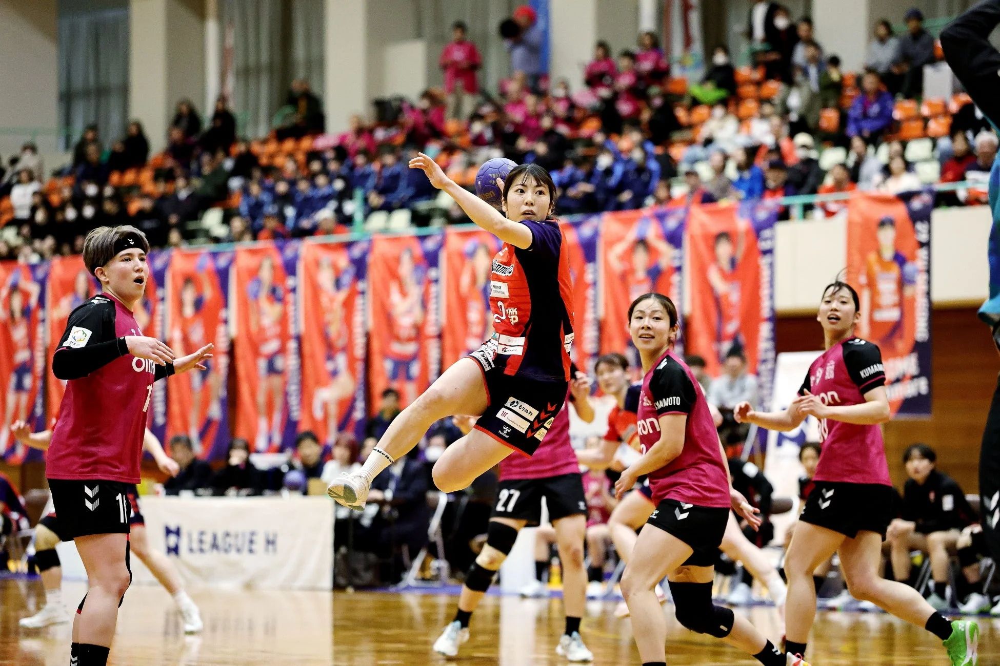 ハンドボールの試合中、赤いユニフォームの選手がジャンプしてボールを投げようとしている決定的な瞬間
