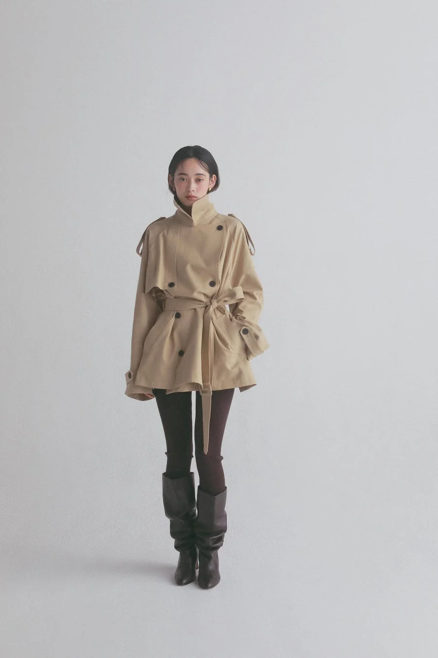 ベージュのショート丈トレンチコートとロングブーツを着用した女性