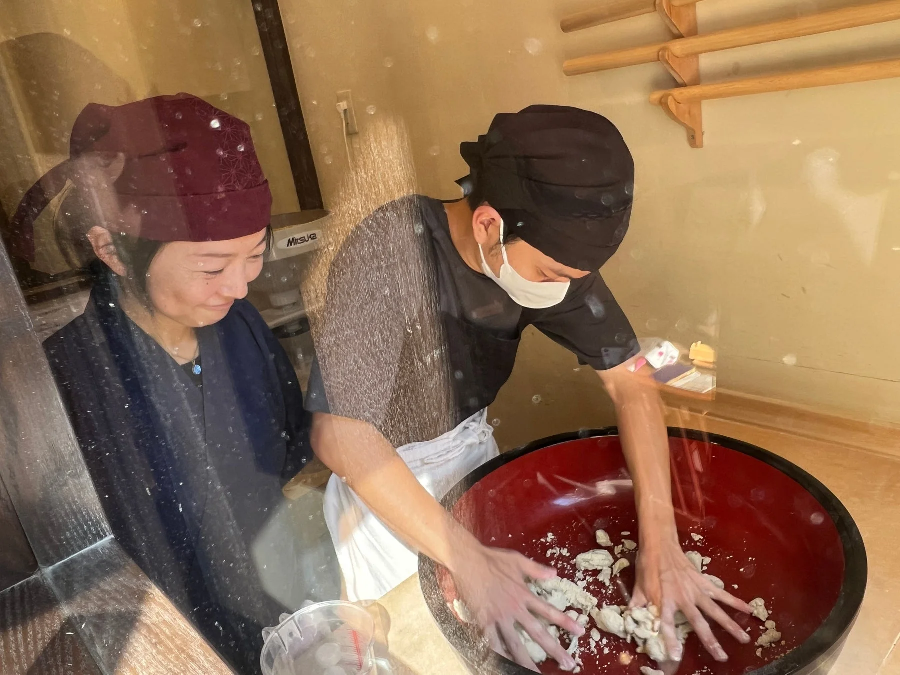 職人が大きな赤いボウルで生地を捏ねている様子を女性が見守っている