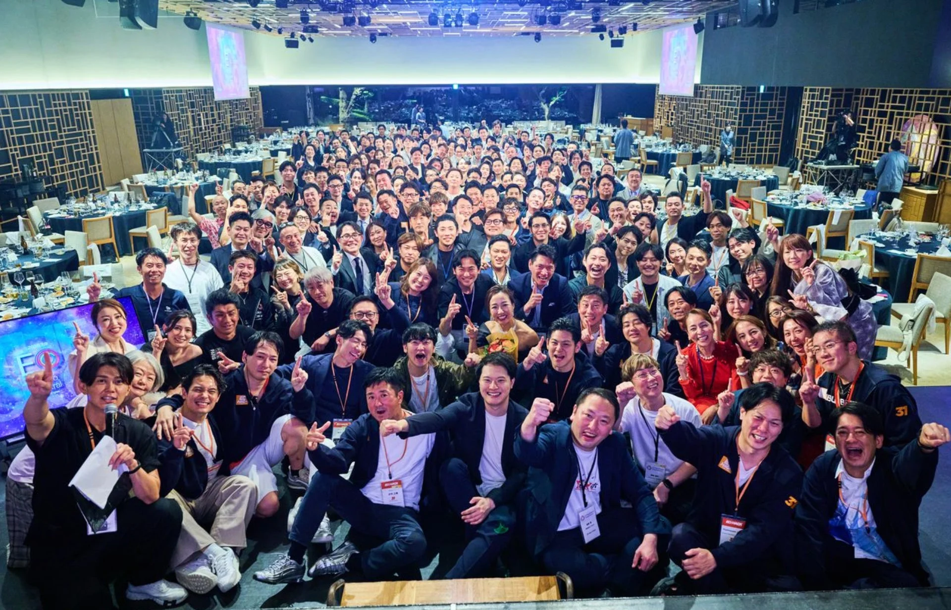 広々とした会場で大勢の参加者が笑顔でポーズをとる集合写真。企業イベントや祝賀会のような活気ある雰囲気で、皆が楽しそうにしている様子が伝わります。
