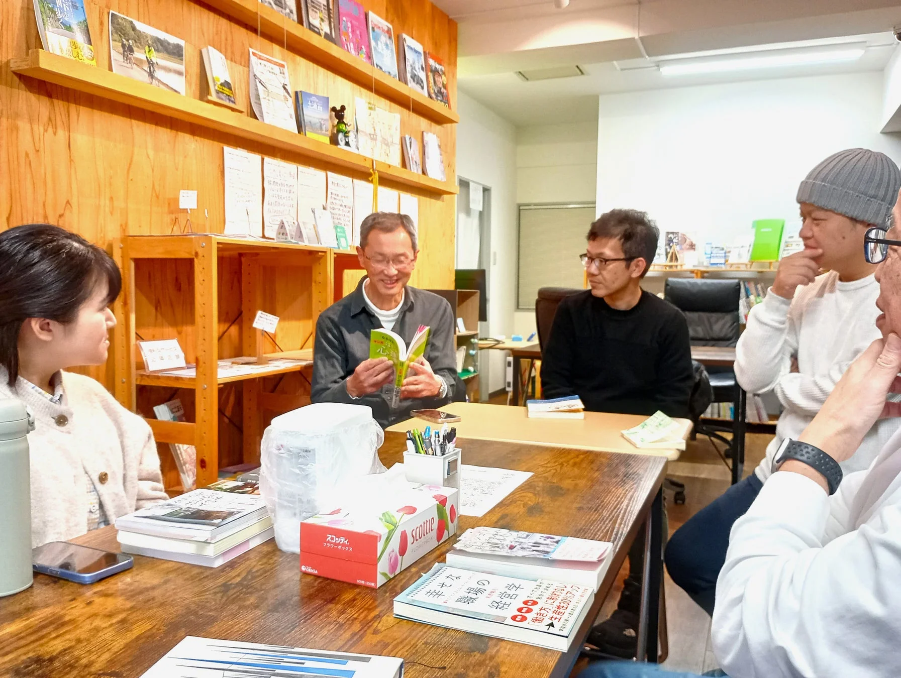 本を読みながら笑顔で話す男性と、それを取り囲む人々