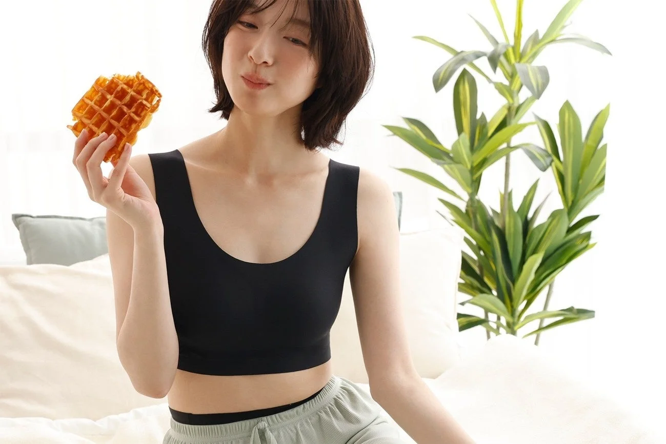 黒いブラトップとリラックスウェアを着た女性が、ワッフルを手に微笑んでいる