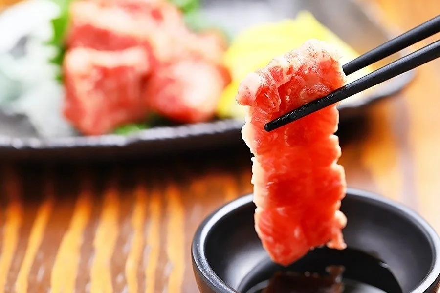 箸で馬肉をタレにつける様子