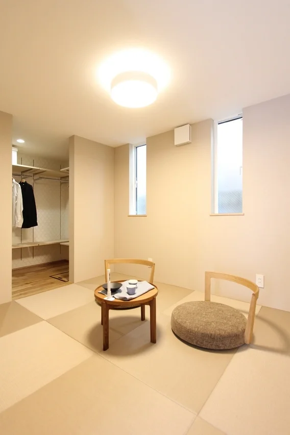 モダンな和室インテリアで、市松模様の畳が敷かれた部屋です。中央にはローテーブルと低い椅子が配置され、奥にはオープンな収納スペースが見えます。シンプルで落ち着いた雰囲気の空間です。