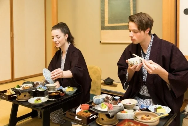 伝統的な和室で着物を着た男女が、美しい盛り付けの日本料理を楽しんでいます。
