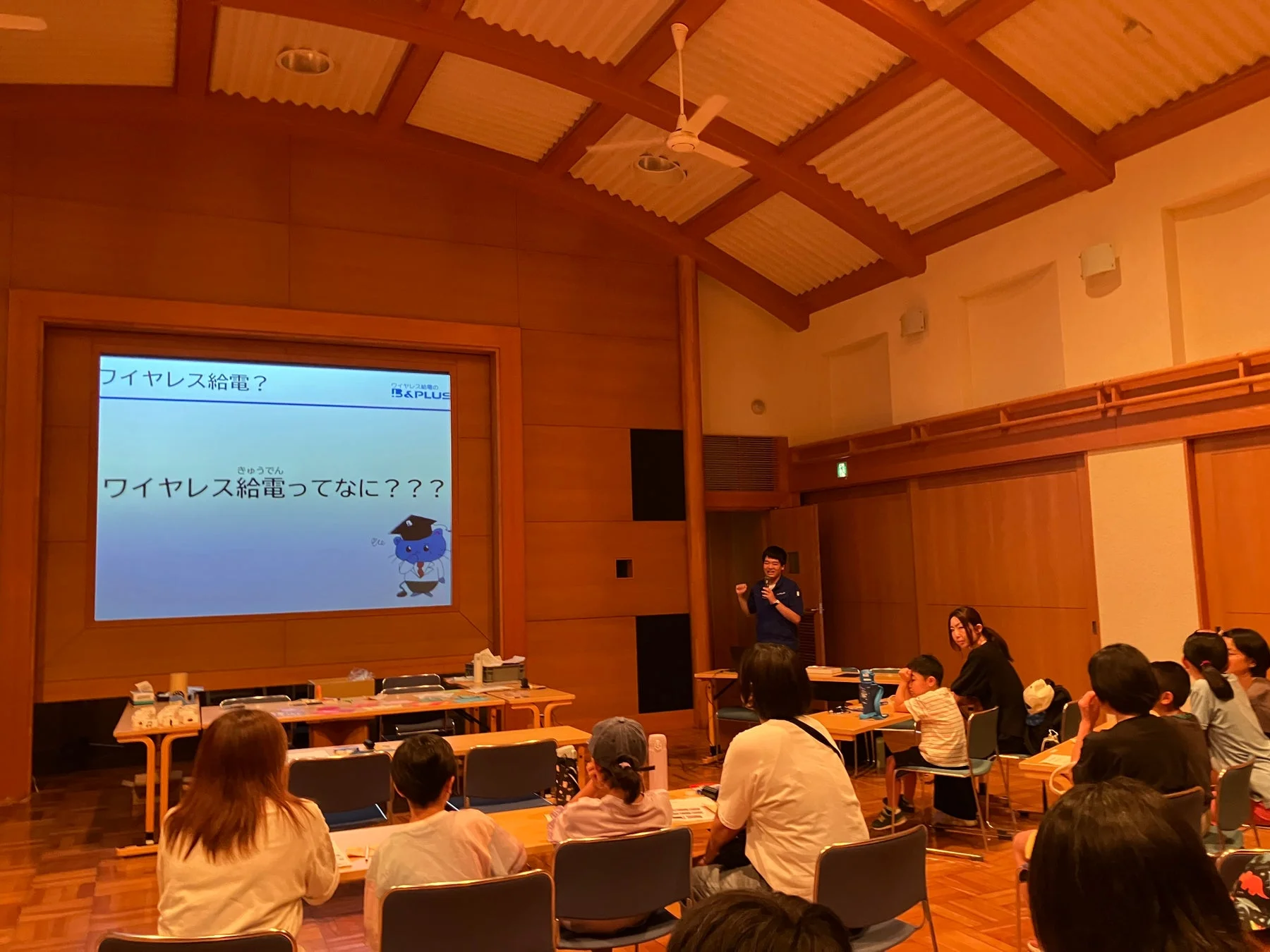 ワイヤレス給電ってなに？の説明をするスタッフと聞く子どもたち