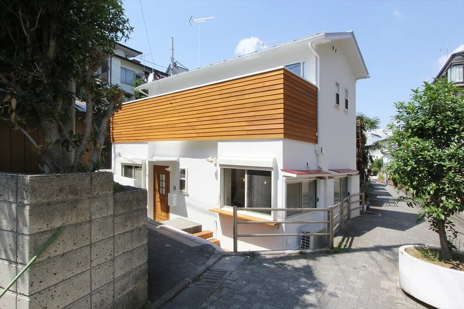 坂道に建つ白い外壁と木目調のアクセントが特徴的なモダンな一軒家。