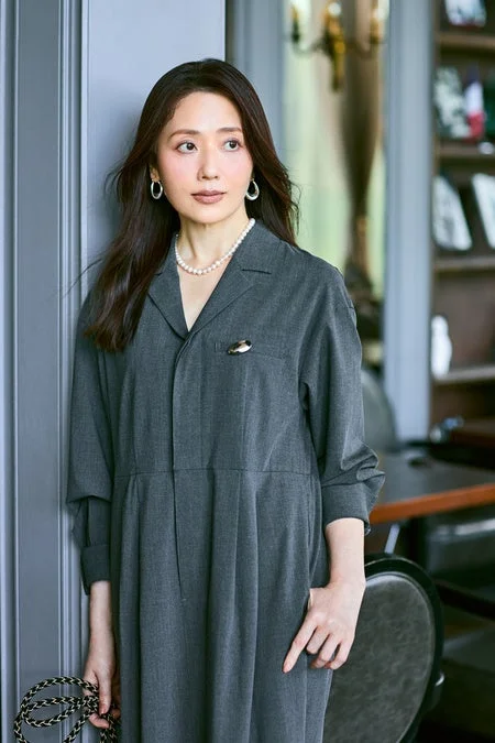 灰色のロングワンピースを着用し、パールネックレスとイヤリングを身につけた女性のポートレート。