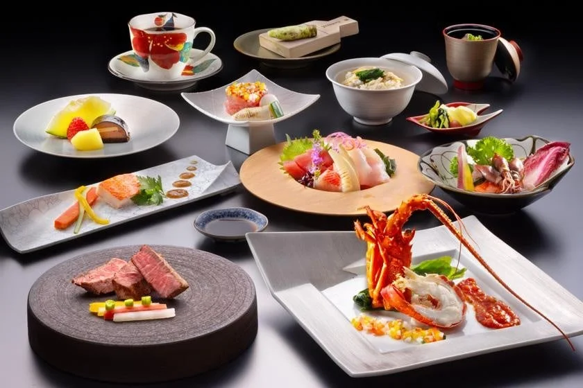 黒い背景に、伊勢海老、刺身、ステーキ、デザートなど、美しく盛り付けられた豪華な和食の会席料理