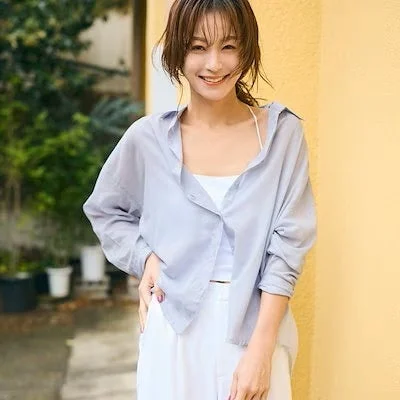 笑顔でカメラを見つめる若い女性のポートレート。薄いブルーのシャツと白いパンツを着用したカジュアルな夏の装い。背景には緑と黄色の壁。