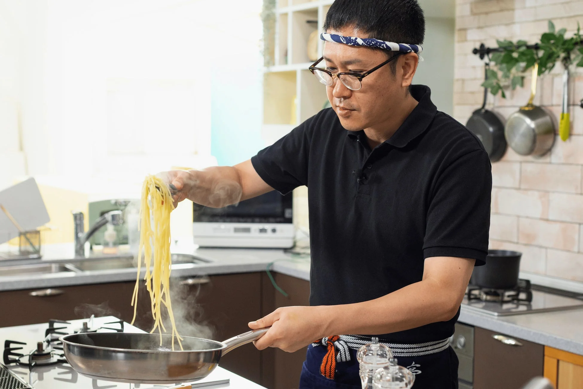 鉢巻を巻いた男性がキッチンでパスタを調理している様子