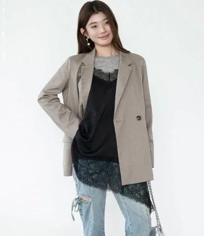白い背景の前で微笑む女性が写っています。ベージュのブレザーにグレーのTシャツ、黒いレース付きキャミソールを重ね着し、ダメージデニムを合わせたきれいめカジュアルなスタイルです。パールイヤリングがアクセントになっています。