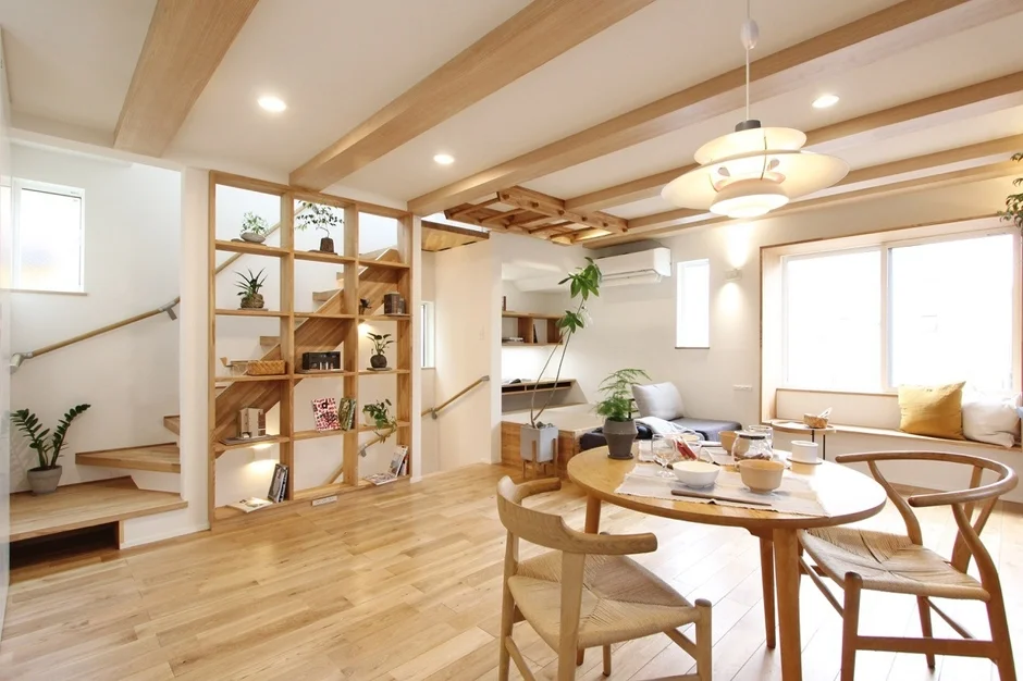 木材を多用した明るく開放的なリビングダイニング。オープンシェルフや階段があり、観葉植物が配置された心地よい空間です。