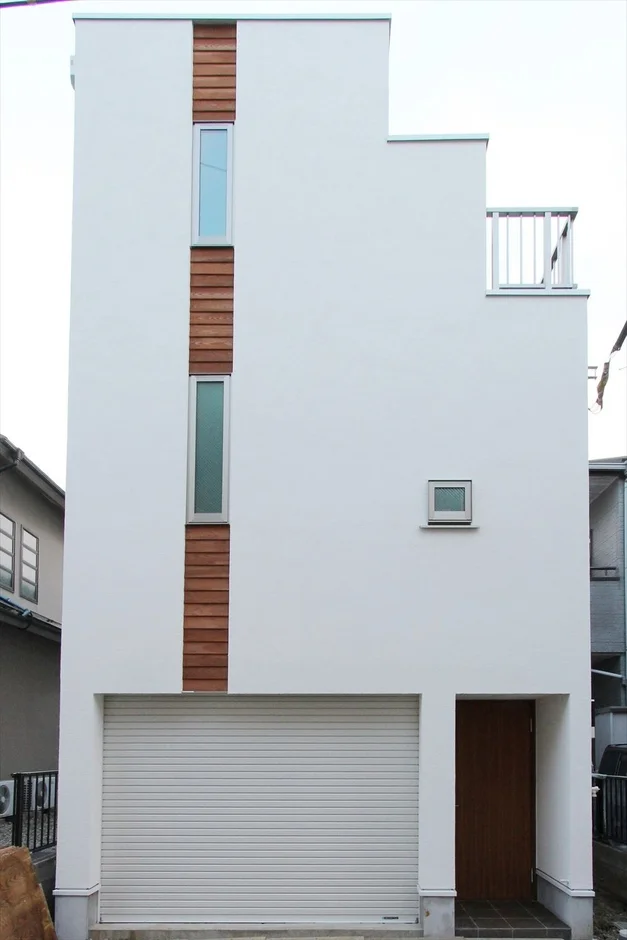白い外壁と木目調のアクセントが特徴的な、現代的で縦長の狭小住宅です。