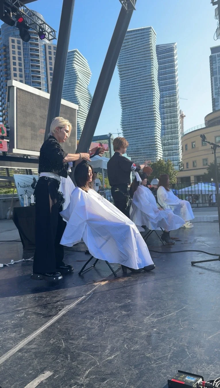 屋外ステージで美容師が客の髪を切るヘアカットイベントの様子