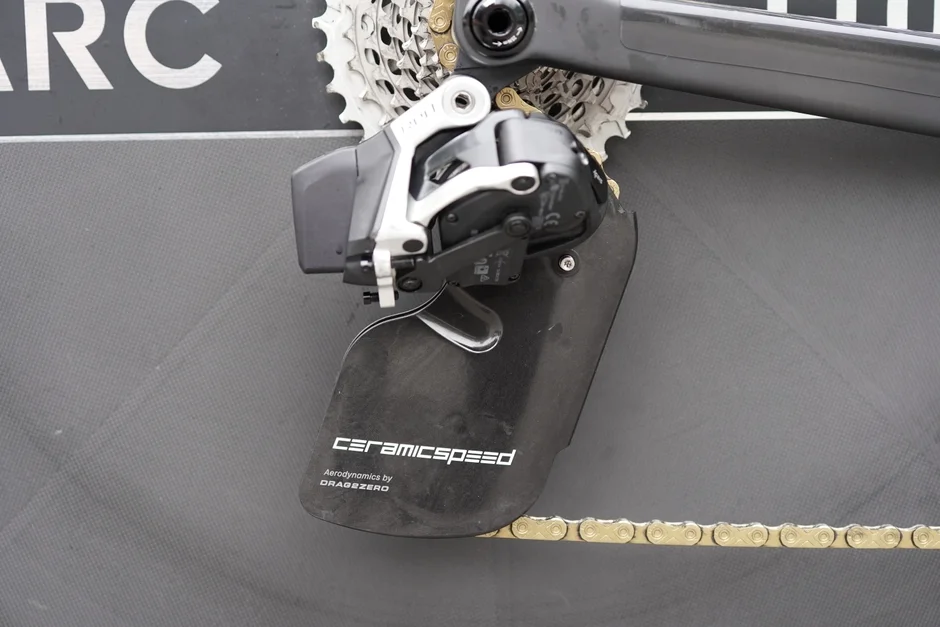 自転車の高性能なリアディレイラーとカセットスプロケット、ゴールドのチェーンが写っています。セラミックスピード製の大型プーリーケージシステムが特徴で、空力性能が重視されたパーツです。