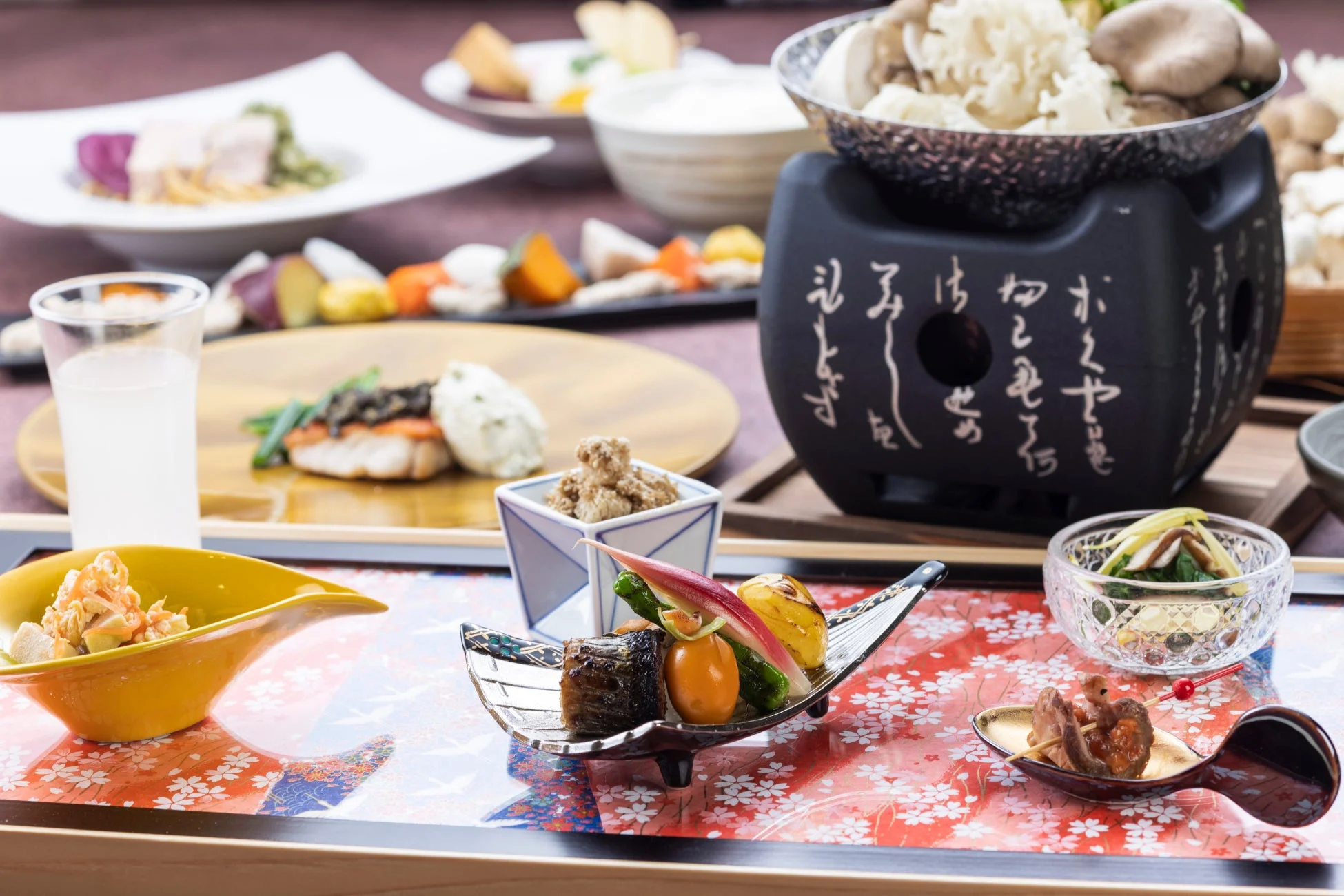 日本の伝統的な会席料理が美しく並べられた食卓。色とりどりの小鉢や煮物、焼き物などが様々な器に盛り付けられ、中央にはきのこ鍋が置かれている。上品で豪華な食事の風景。