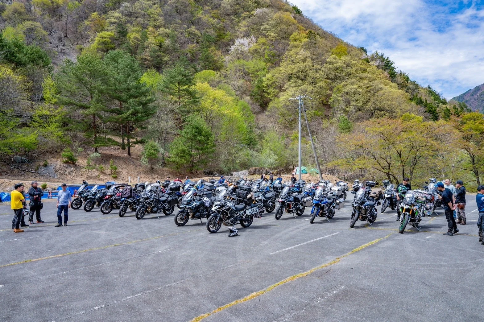 多数のバイクが山間の駐車場に駐車され、ライダーたちが集まっている様子