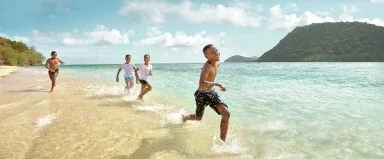 青い海と白い砂浜で、数人の子供たちが楽しそうに波打ち際を走っている様子