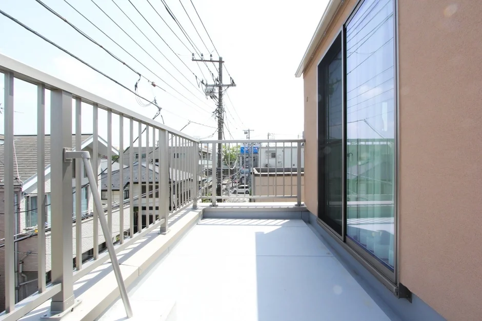 広々としたバルコニーから、電線が張り巡らされた住宅街を見下ろす風景。明るい日差しが差し込み、開放的な雰囲気が感じられます。