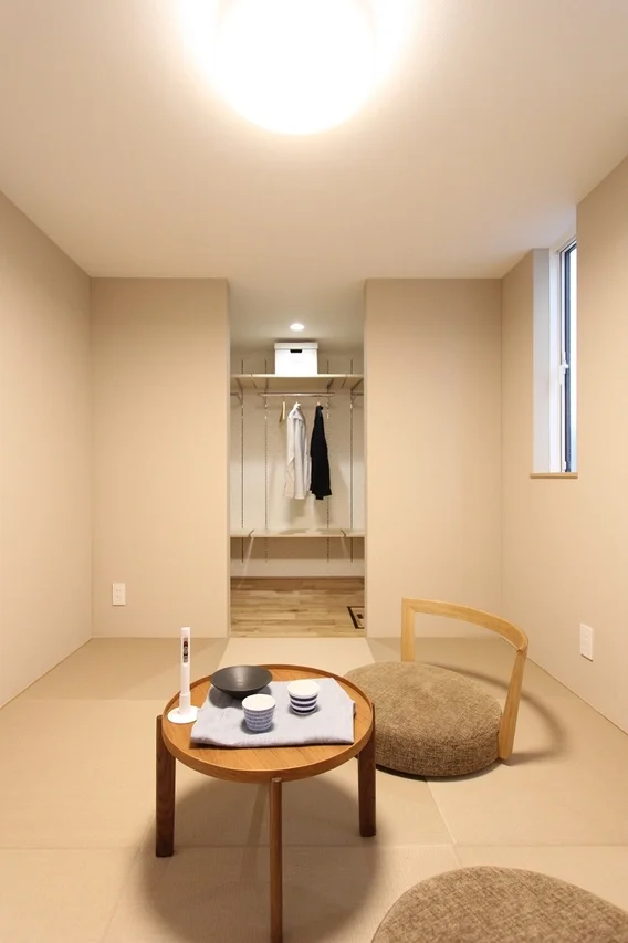 畳敷きのシンプルで落ち着いた雰囲気の部屋です。中央には木製のローテーブルに茶器が置かれ、モダンな座椅子が配されています。奥にはオープンクローゼットが見え、機能的な空間が広がっています。