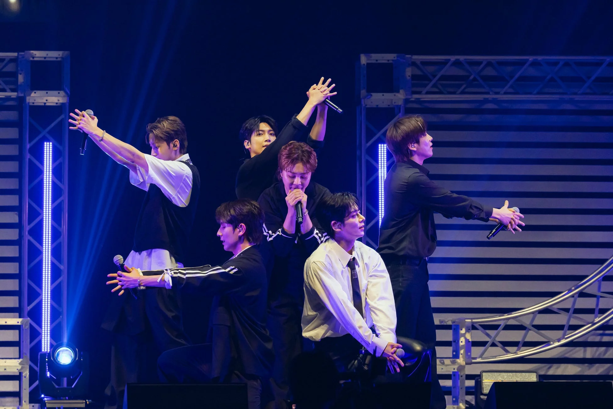 青い照明が印象的なステージで、6人組の男性アイドルグループがマイクを手にパフォーマンスしている様子。メンバーは黒と白の衣装を着用しており、ライブ中の熱気と一体感が伝わる一枚です。