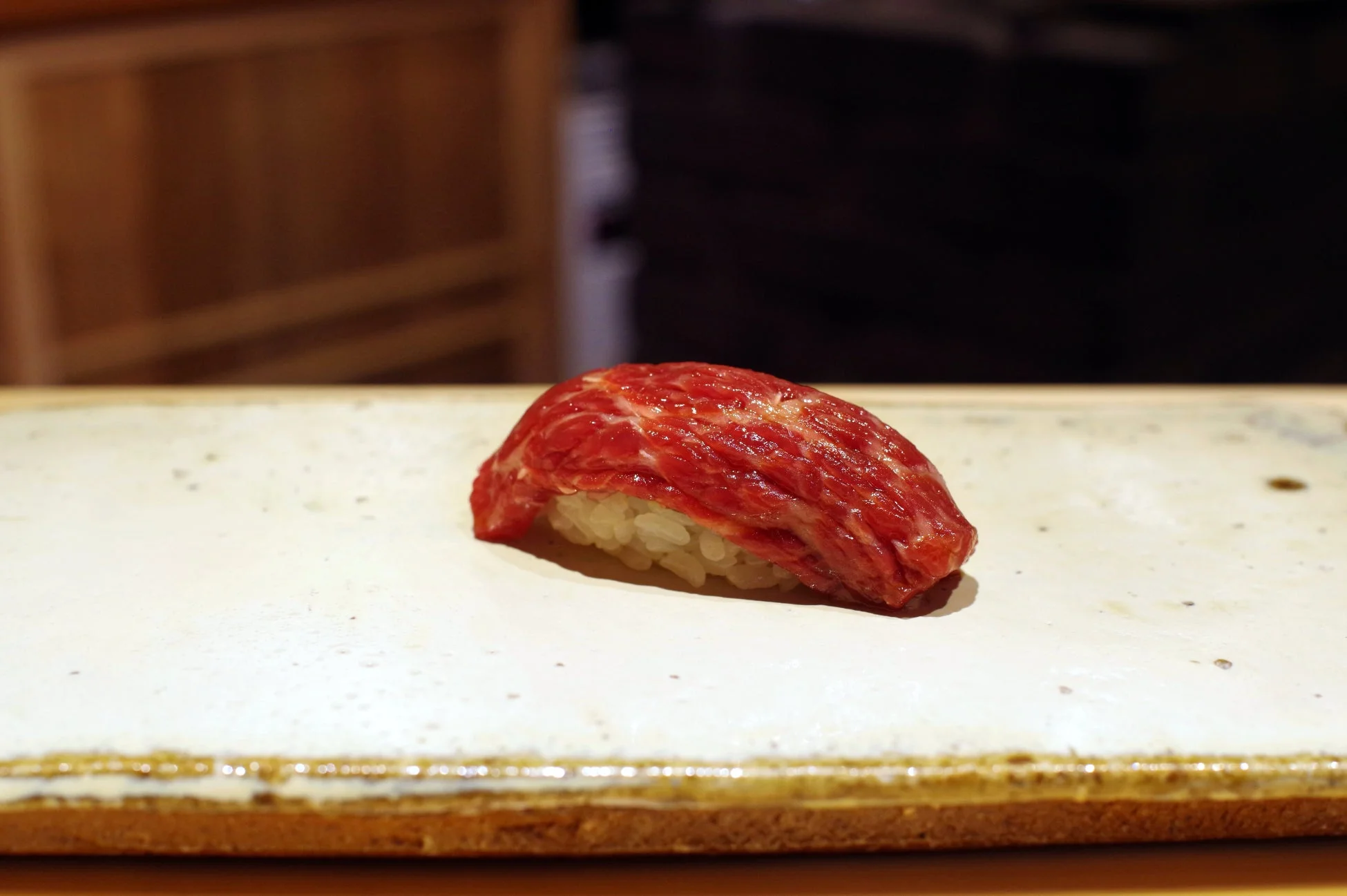 美しい霜降りの入った鮮やかな赤色の和牛が、白いシャリの上にのせられた一貫の握り寿司