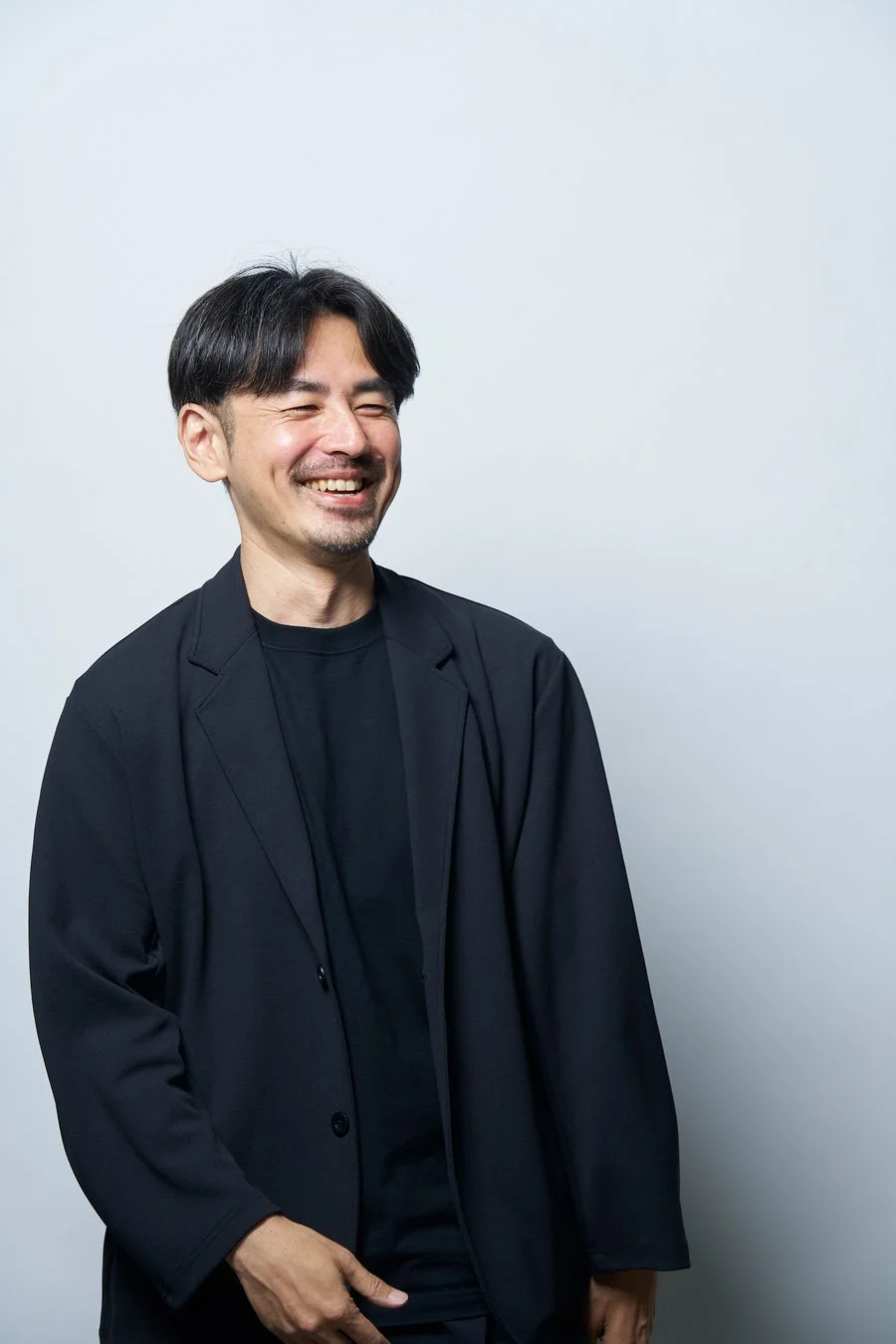 黒いジャケットとTシャツを着て笑顔を見せるアジア人男性