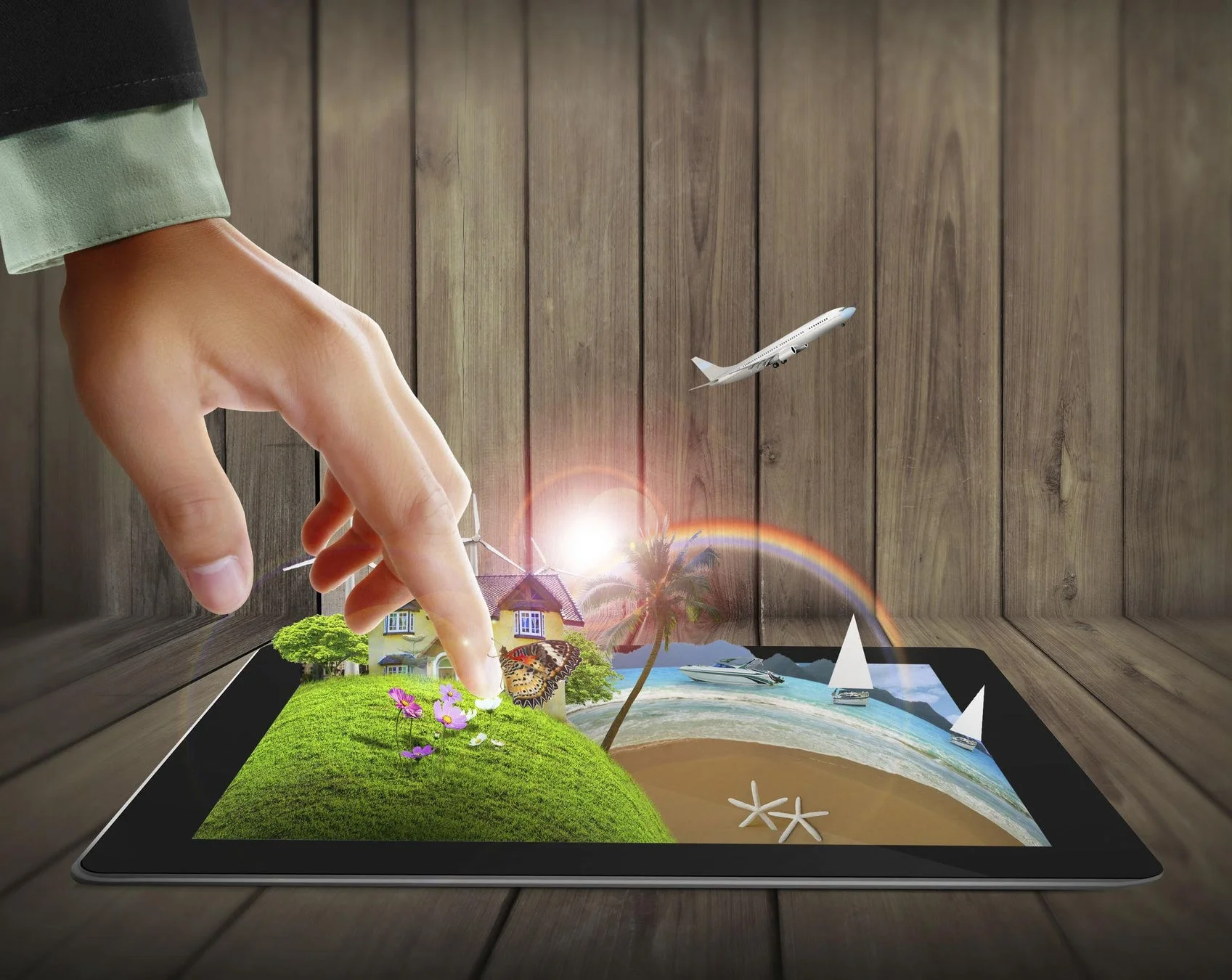 手がタブレットを操作し、画面から家、緑豊かな丘、ビーチ、海、飛行機、虹といった鮮やかな風景が飛び出しているような合成画像。デジタルで広がる夢や旅行のイメージを表現しています。