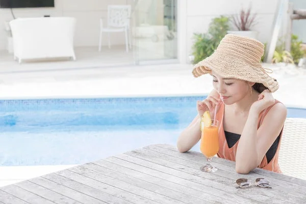 プールサイドで麦わら帽子をかぶりドリンクを飲む女性