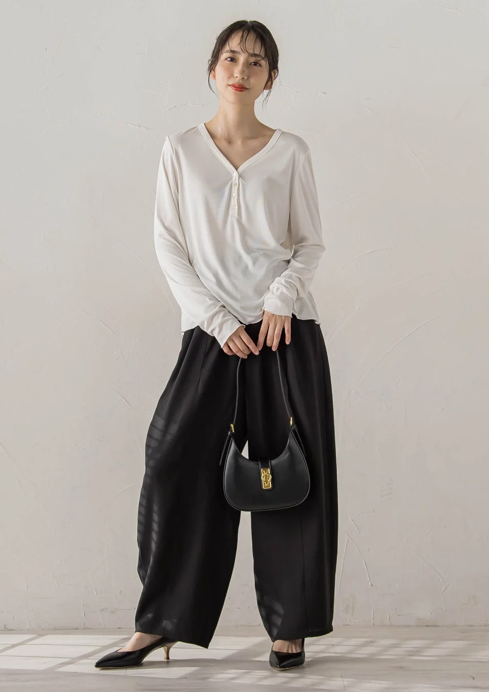 白いVネック長袖トップスと黒のワイドパンツを着用した女性
