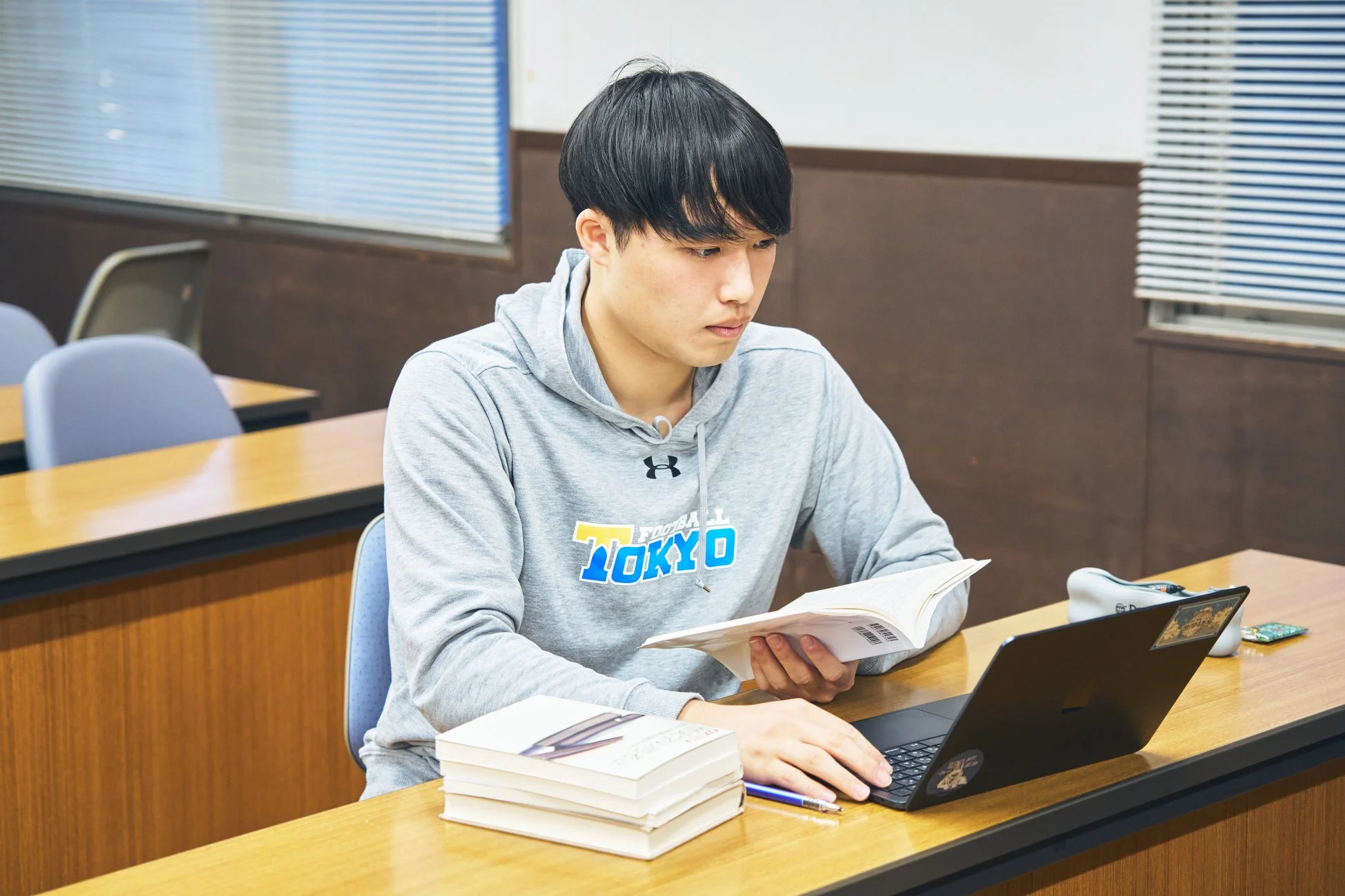 教室でノートパソコンと本を使って勉強している若い男性