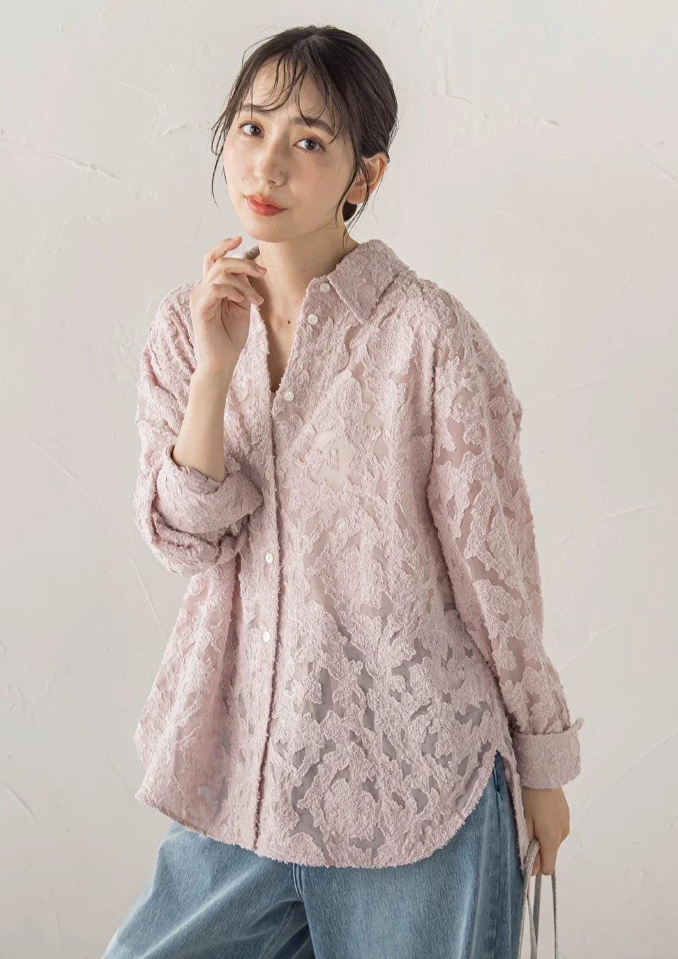 淡いピンクの透け感のある長袖シャツとデニムパンツを着用した若い日本人女性
