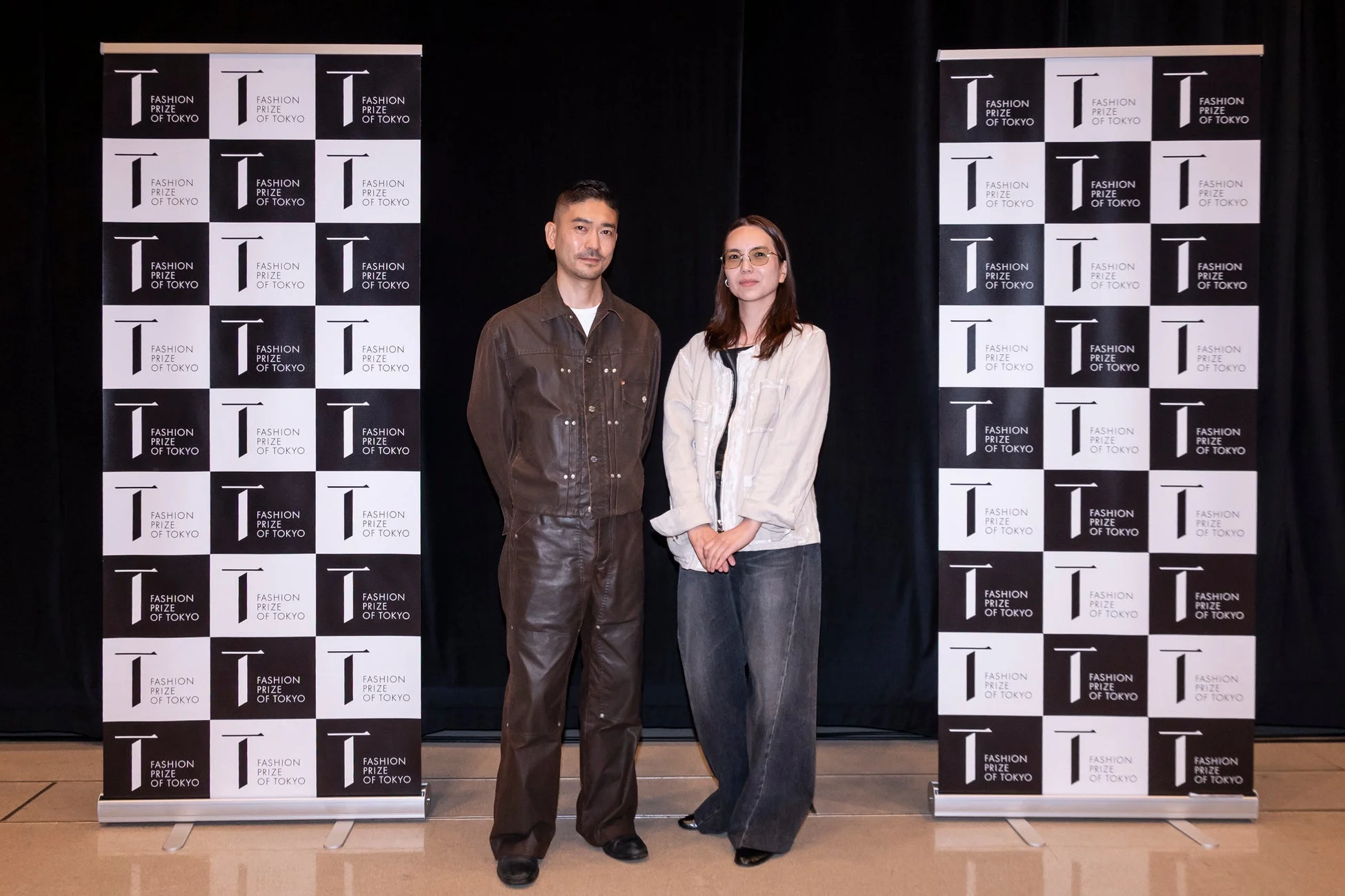 FASHION PRIZE OF TOKYOのロゴが並ぶ背景の前で、男女2人が並んで立っている