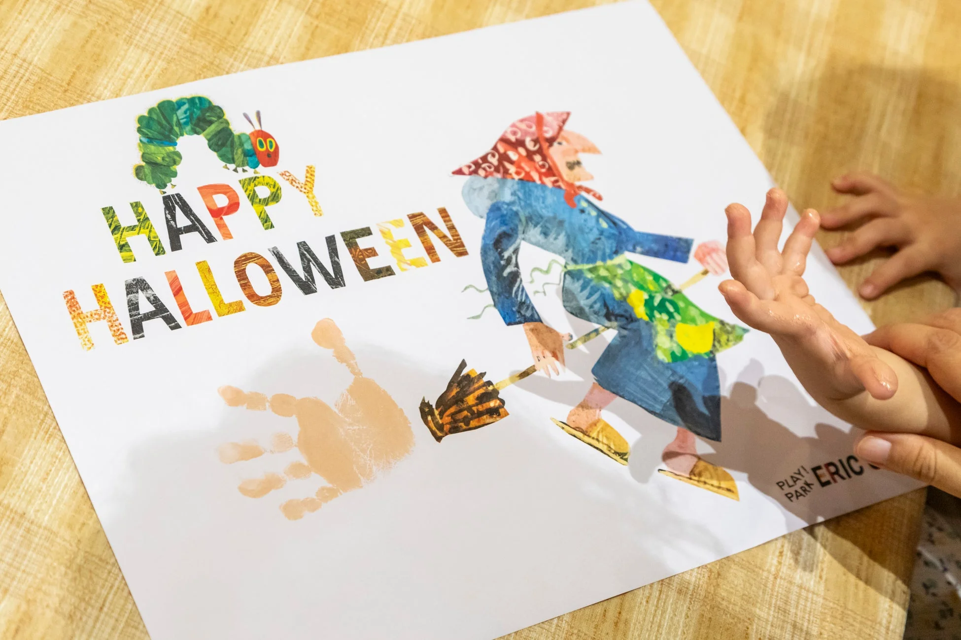 「はらぺこあおむし」と魔女が描かれた「HAPPY HALLOWEEN」のポスターに、子供の手形が押されている様子です。