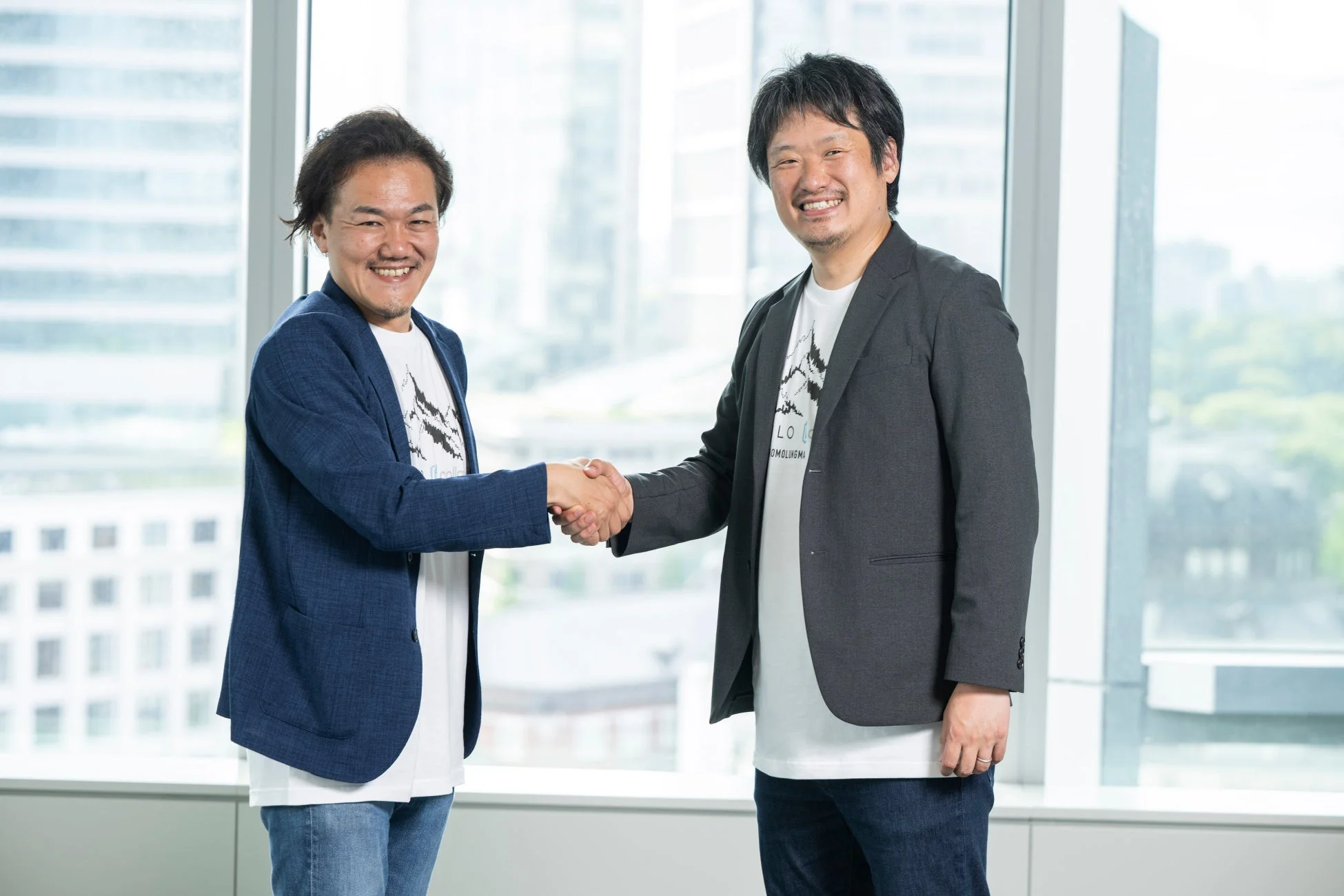 明るいオフィスで二人の男性が笑顔で握手を交わしている。ビジネス上の提携や合意を象徴する一枚で、和やかな雰囲気が伝わる。
