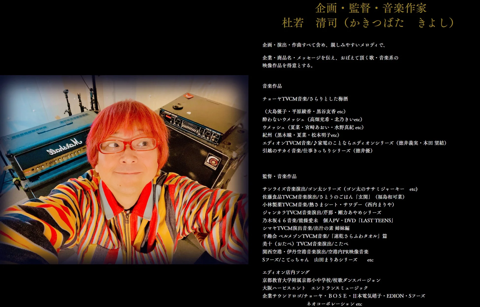 赤い髪とメガネが特徴的な音楽作家、杜若清司氏の自撮り写真。カラフルな服を着用し、背景にはマーシャルアンプを含む音楽機材が見える。右側には氏の企画・監督・音楽作品のリストが記載されている。