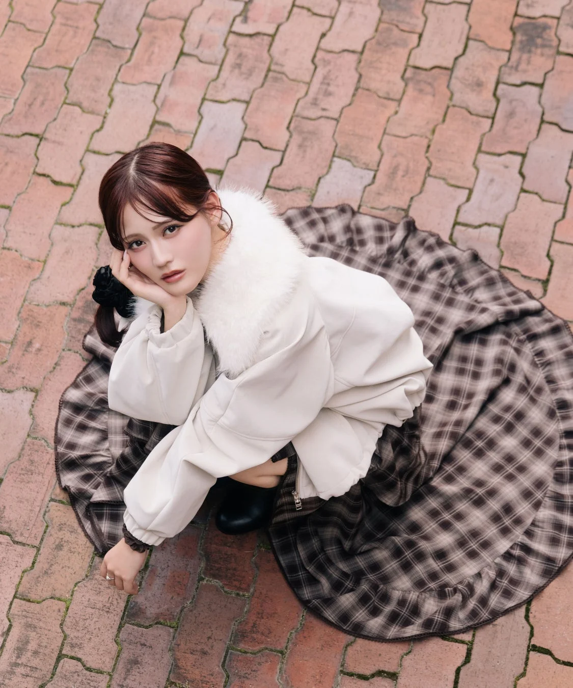 レンガ調の地面に座り込み、カメラを見つめる若い女性のポートレート。