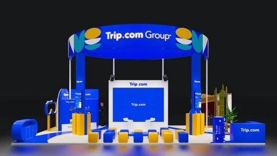 Trip.com Groupのロゴが特徴的な、青と黄色を基調としたモダンな展示ブースの様子。中央に大きなスクリーンがあり、ブランド名が表示され、来場者向けの座席も配置されている。
