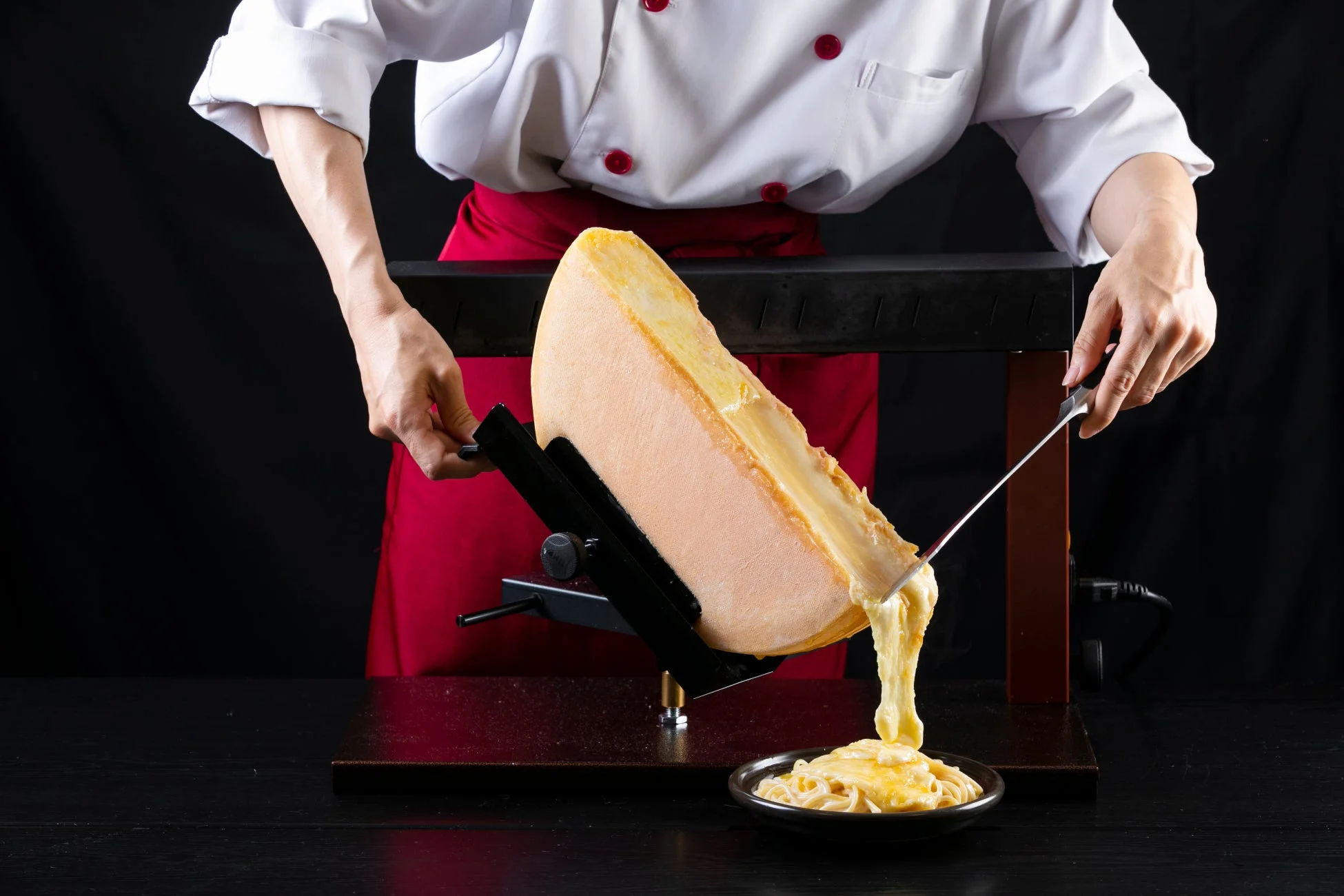 シェフがラクレットチーズをパスタにかけている様子