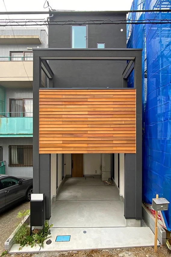 都心部の狭小敷地に建てられた、ダークグレーの外壁と木目調のアクセントが特徴的なモダンなガレージハウス