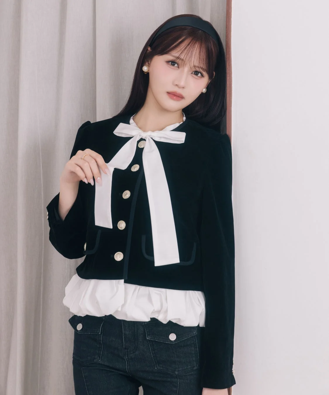 黒いショート丈ジャケットに白い大きなリボンとフリルブラウスを合わせた女性が写っています。