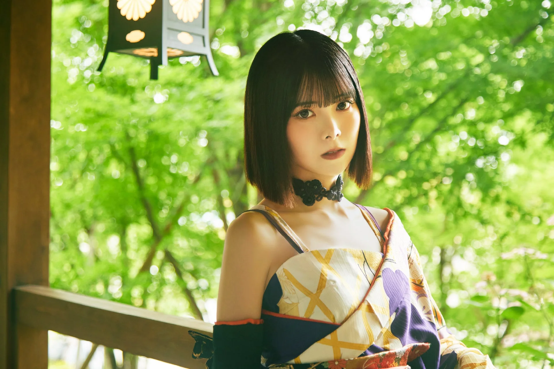 緑豊かな背景を背に、和装の女性がカメラを見つめているポートレートです。