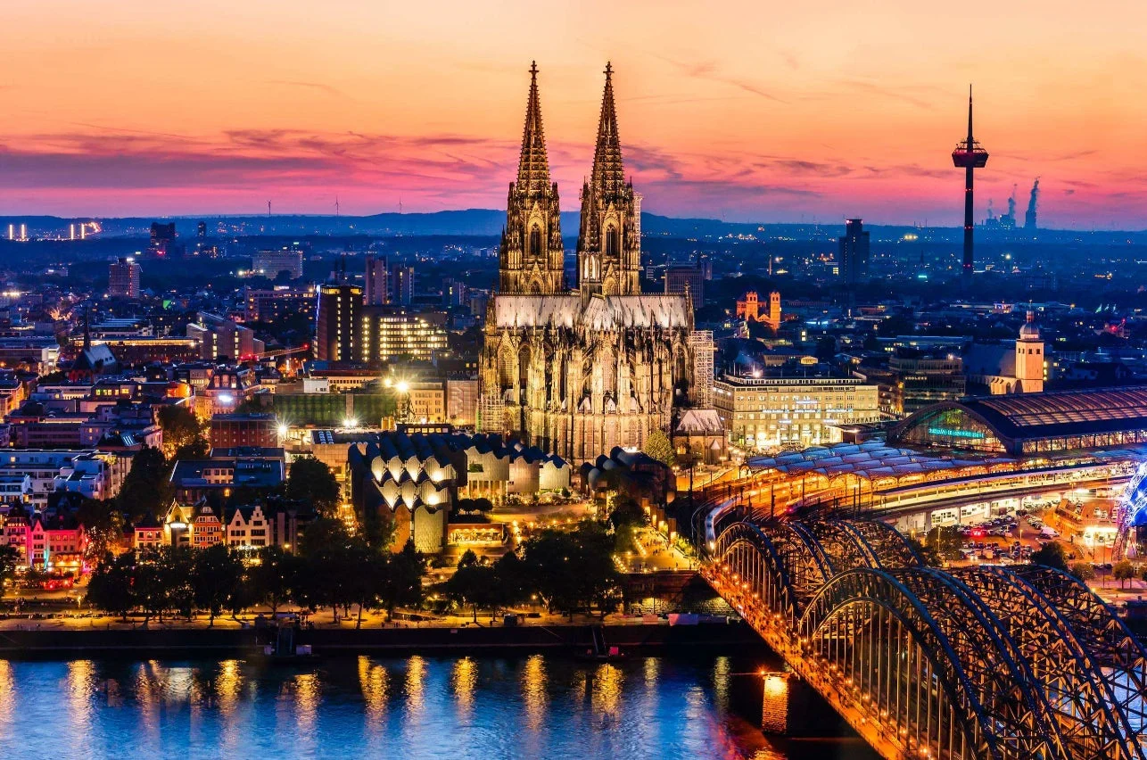 夕焼け空を背景に、ライトアップされたケルン大聖堂、ホーエンツォレルン橋、ライン川が輝くドイツ・ケルンの美しい街並みの夜景