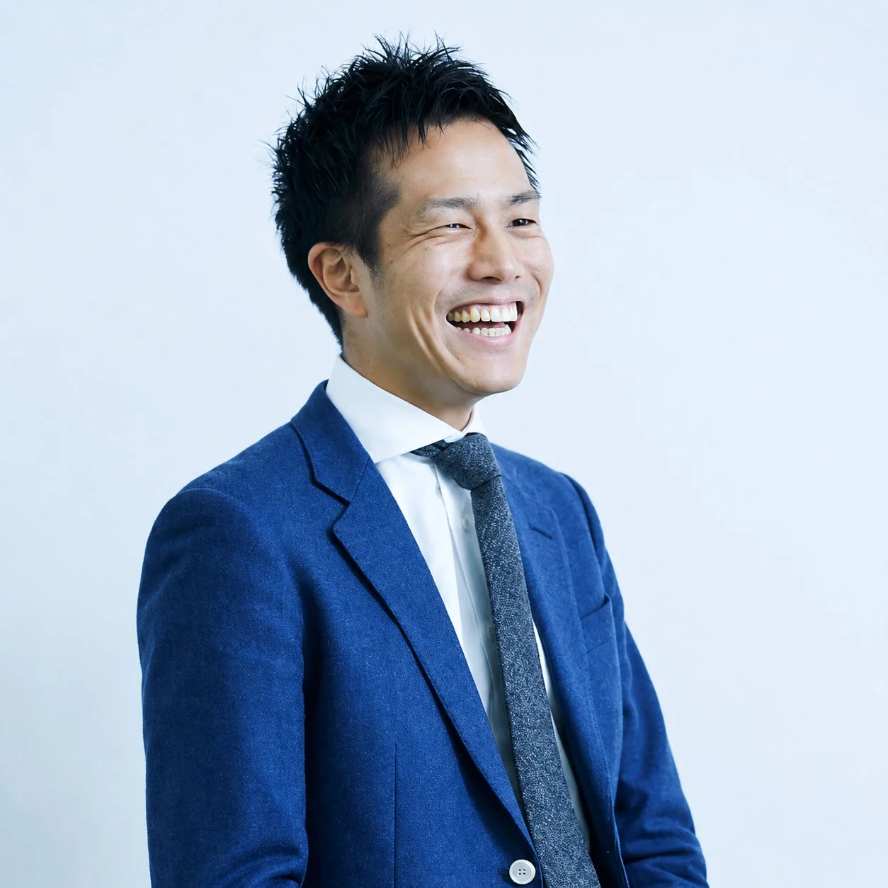 青いスーツと白いシャツを着用し笑顔の日本人男性